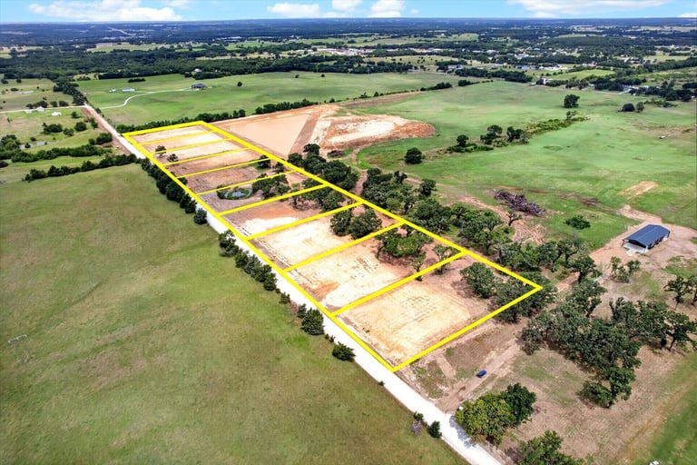 Aerial view of rural land development with marked property sections outlined in yellow, surrounded by green farmland and scattered trees