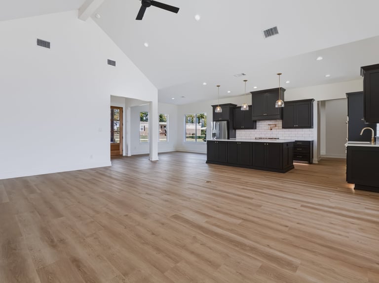 Modern open-concept kitchen and living area with wood flooring, black cabinetry, and white countertops