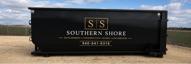 Black dumpster with Southern Shore logo and text in a sandy lot with cloudy sky background