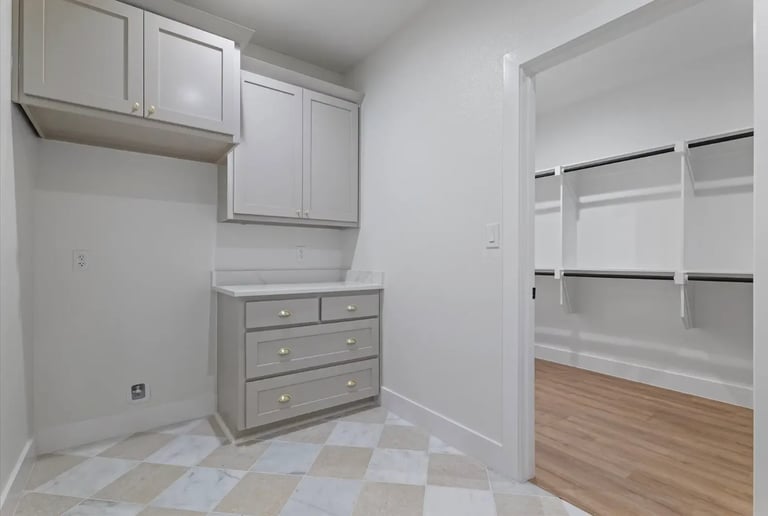 Modern walk-in closet with white cabinetry, gray dresser, checkered floor, and shelving unit with glass doors