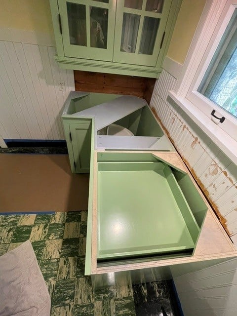 Green kitchen cabinets with open drawers revealing light green interior compartments and white wood frame elements