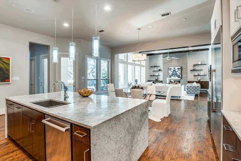 Modern open-concept kitchen with marble island, stainless steel appliances, wooden floors, and contemporary pendant lighting