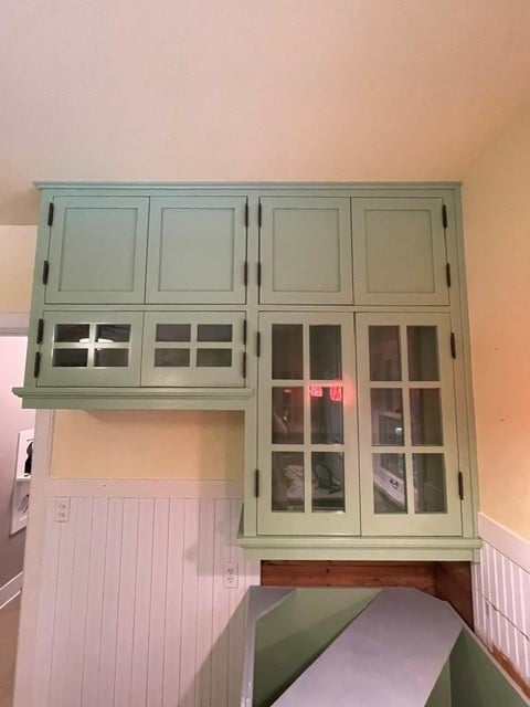 Green wooden cabinet with glass and solid panels mounted on a pale pink and white wall
