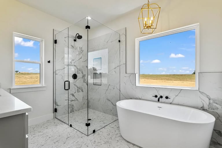 Modern bathroom with white freestanding bathtub, glass walk-in shower with marble surround, and two large windows