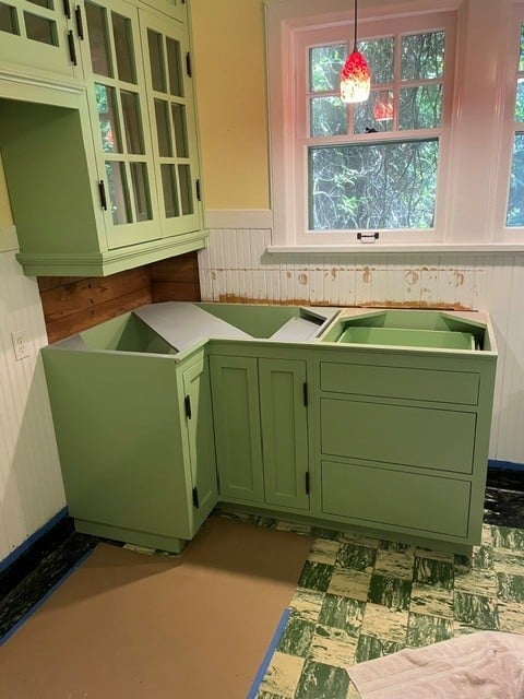 Vintage green kitchen cabinets under renovation in a cottage kitchen with pink window frame and exposed wood details
