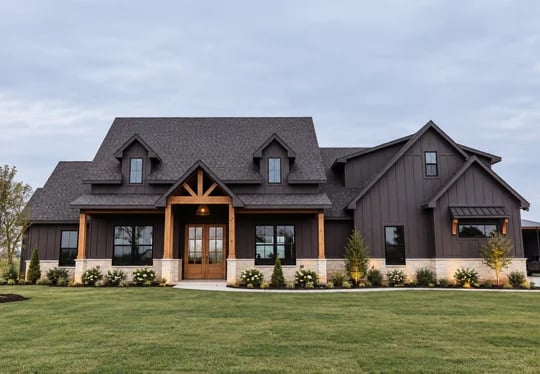 Front elevation of a completed modern farmhouse custom home in Whitesboro, Texas — dark board-and-batten siding with dark window frames, light stone base, two dormers, a natural timber-framed glass entry and completed landscaping with an established lawn