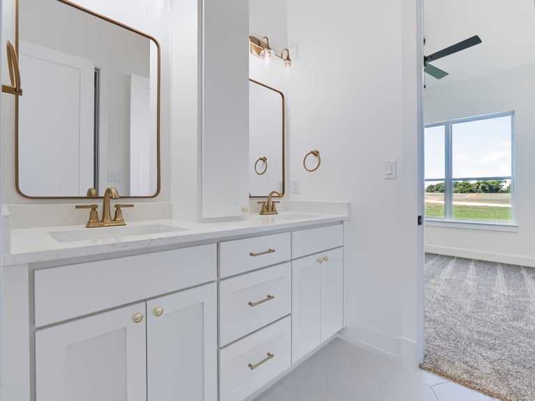 Modern bathroom with white cabinetry, dual brass-framed mirrors, marble countertop, and large windows overlooking landscape