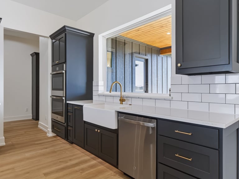 Modern kitchen with black cabinetry, white subway tile backsplash, stainless steel appliances, and farmhouse sink