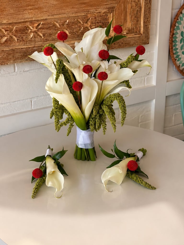 White calla lily bridal bouquet with red berries and green foliage, accompanied by two matching boutonniere corsages on white surface