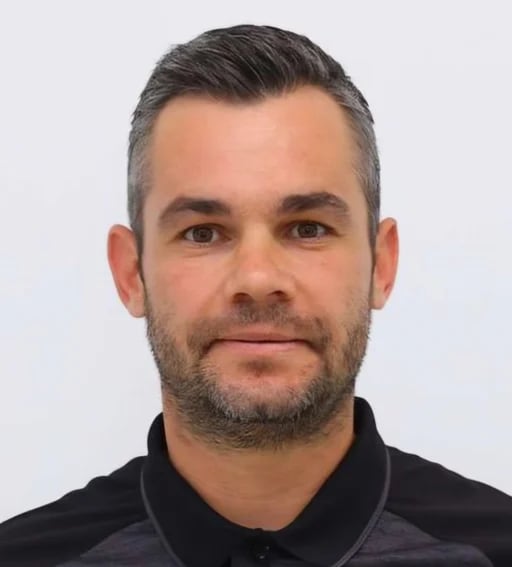 Portrait of a man with dark hair and beard wearing a black collared shirt against a white background