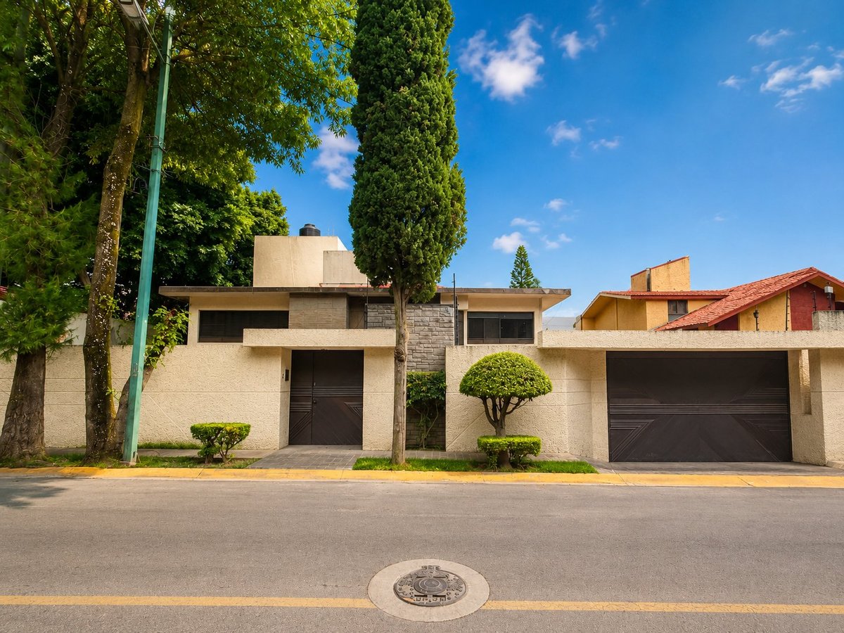 Fachada principal de casa residencial beige moderna con portones oscuros, rodeada de árboles y arbustos