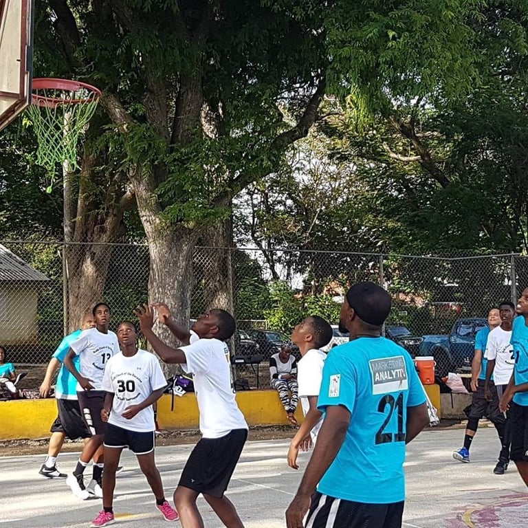 Group of people playing basketball outdoors on a court with trees and fencing in background