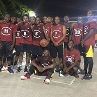 Basketball team in maroon uniforms posing together at night on a street court