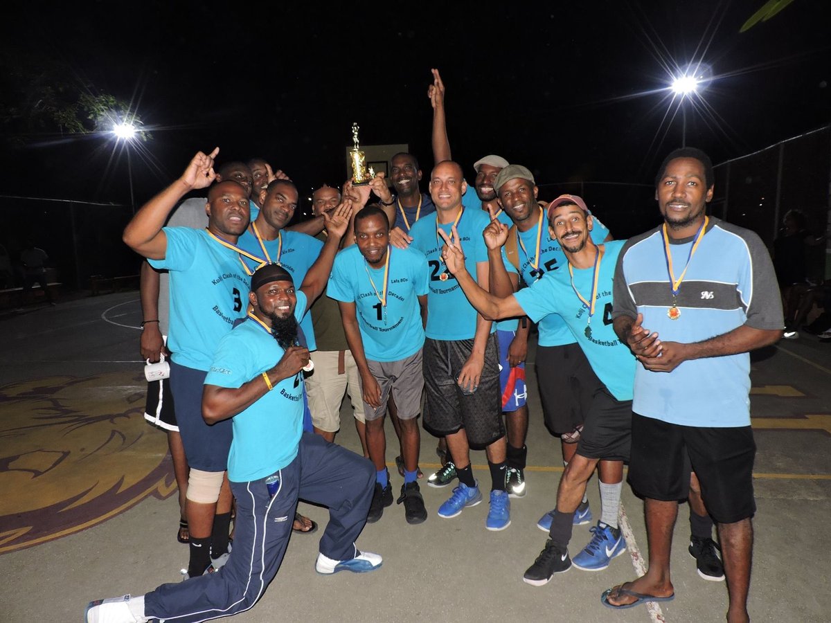 Group of people in blue shirts celebrating with a trophy at night on a basketball court