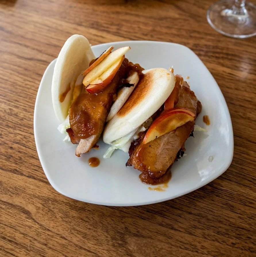 Pork belly sliders on bao buns with apple slaw, served on a wooden table