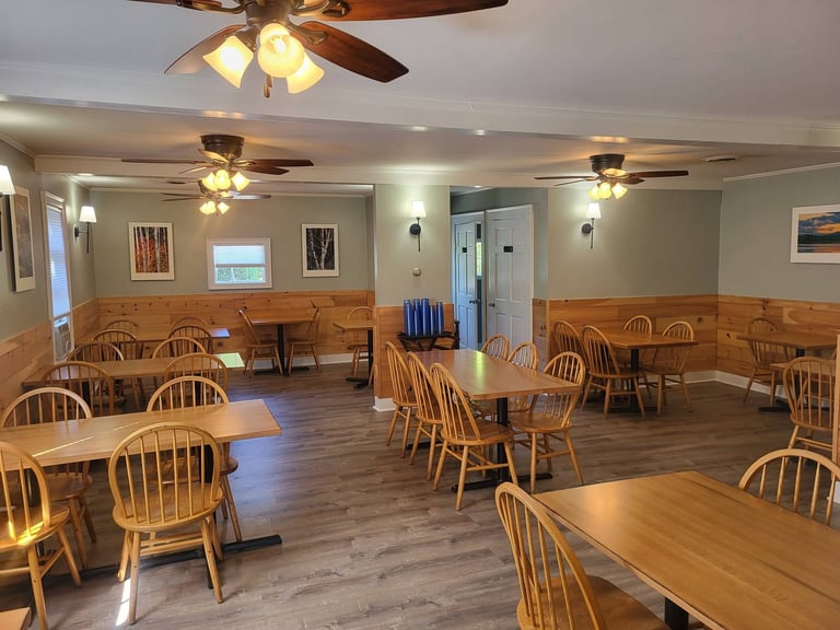 Spacious dining room with multiple wooden tables and Windsor chairs, ceiling fans, and warm lighting