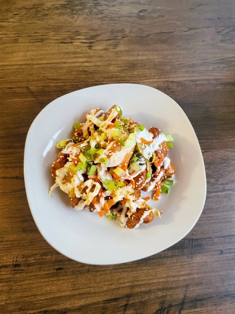 Loaded french fries topped with cheese, sour cream, bacon, and green onions on a white plate on a wooden table