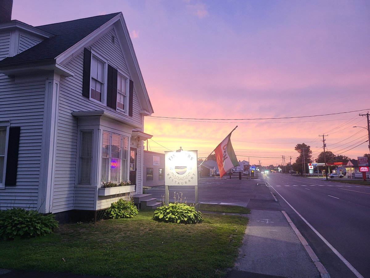 White house with glowing storefront at dusk on rural road with purple and pink sky at sunset