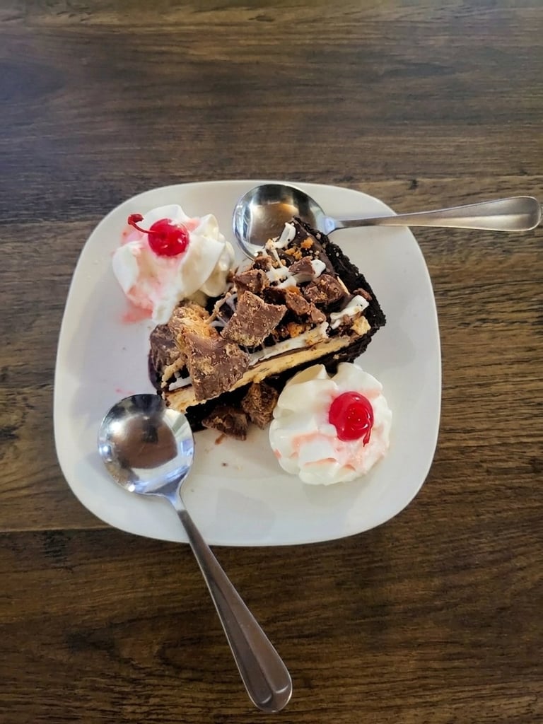 Chocolate cake slice with whipped cream and maraschino cherries on a white plate with spoons