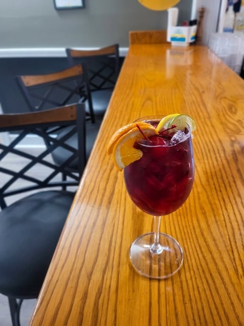 A dark red cocktail with orange citrus garnish