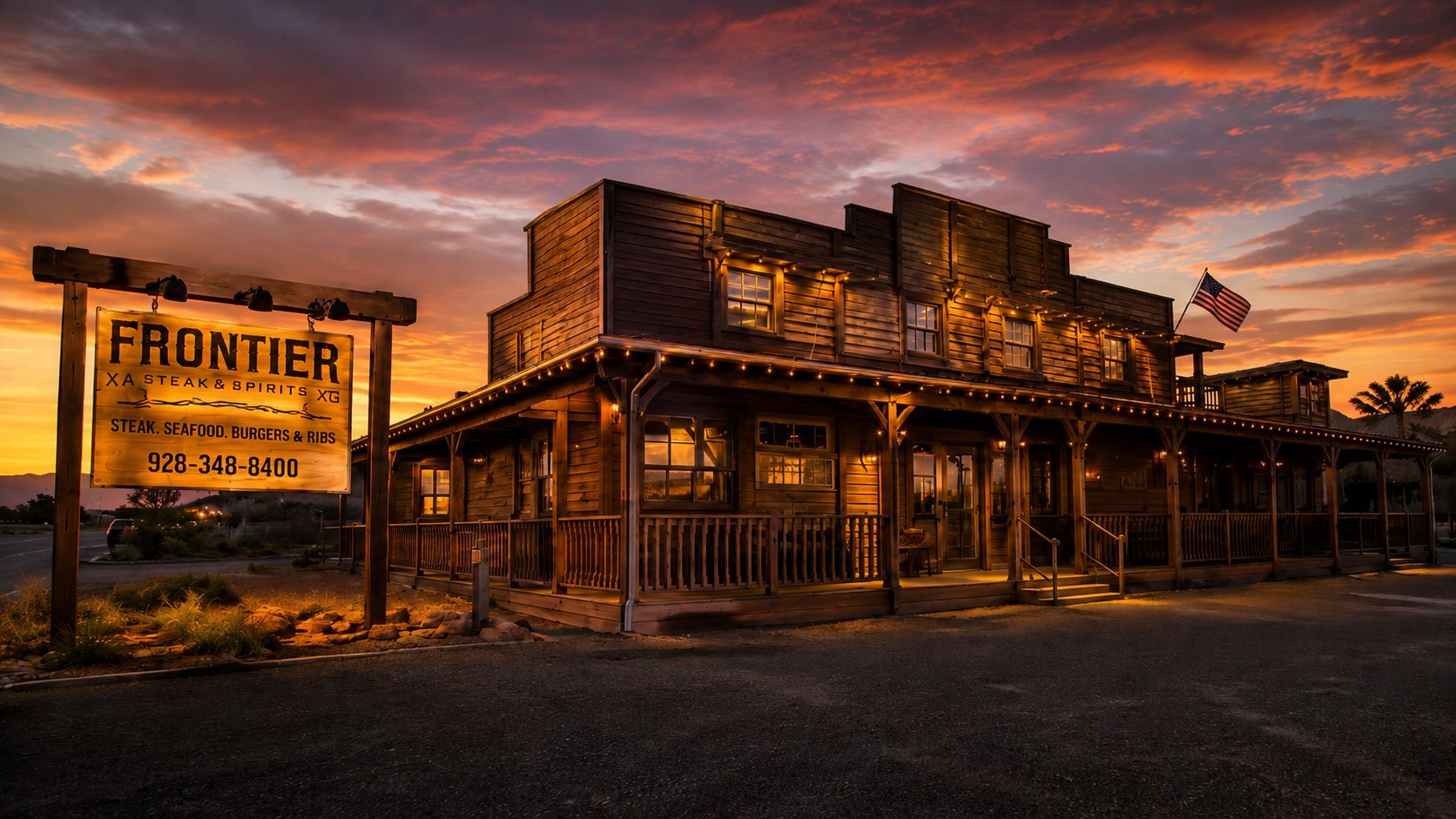 Illuminated Old West-style wooden buildings at dusk with a Frontier sign and dramatic orange sunset sky