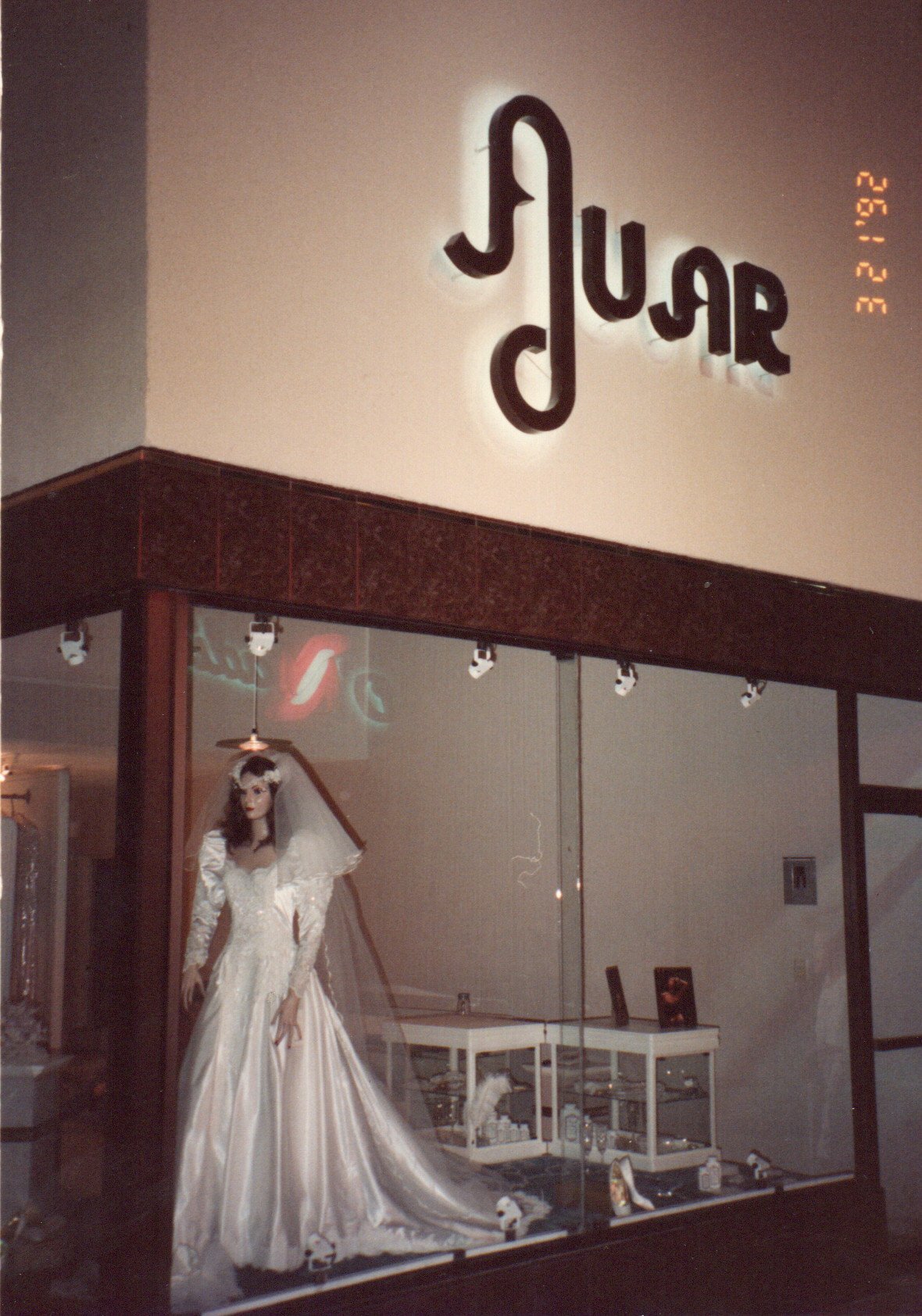 Storefront window display with BLUR neon sign above, featuring a bridal gown on a mannequin against beige walls