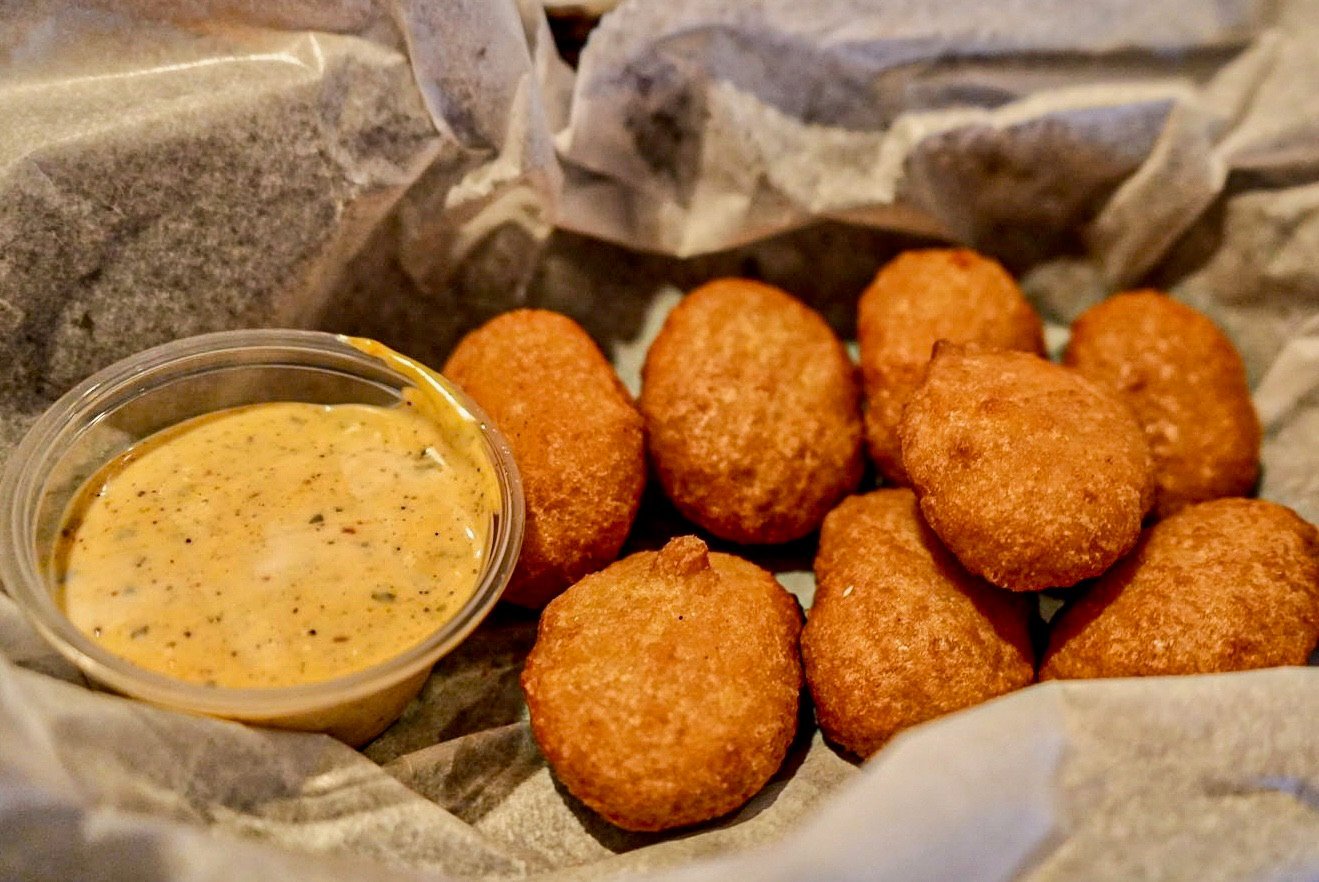 Golden fried hushpuppies in parchment paper with a bowl of creamy dipping sauce