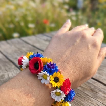 Colorful floral bracelet made of red, yellow, blue, and white flowers worn on a persons wrist outdoors.