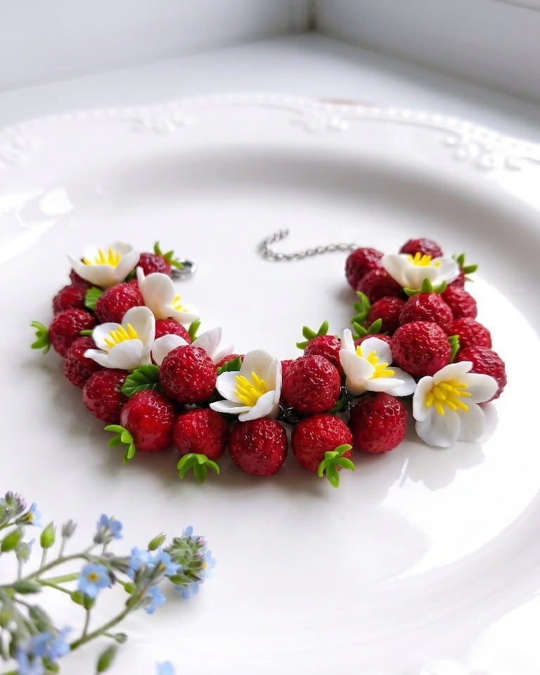Decorative bracelet made of fresh red raspberries and white daisy flowers with yellow centers on a white plate