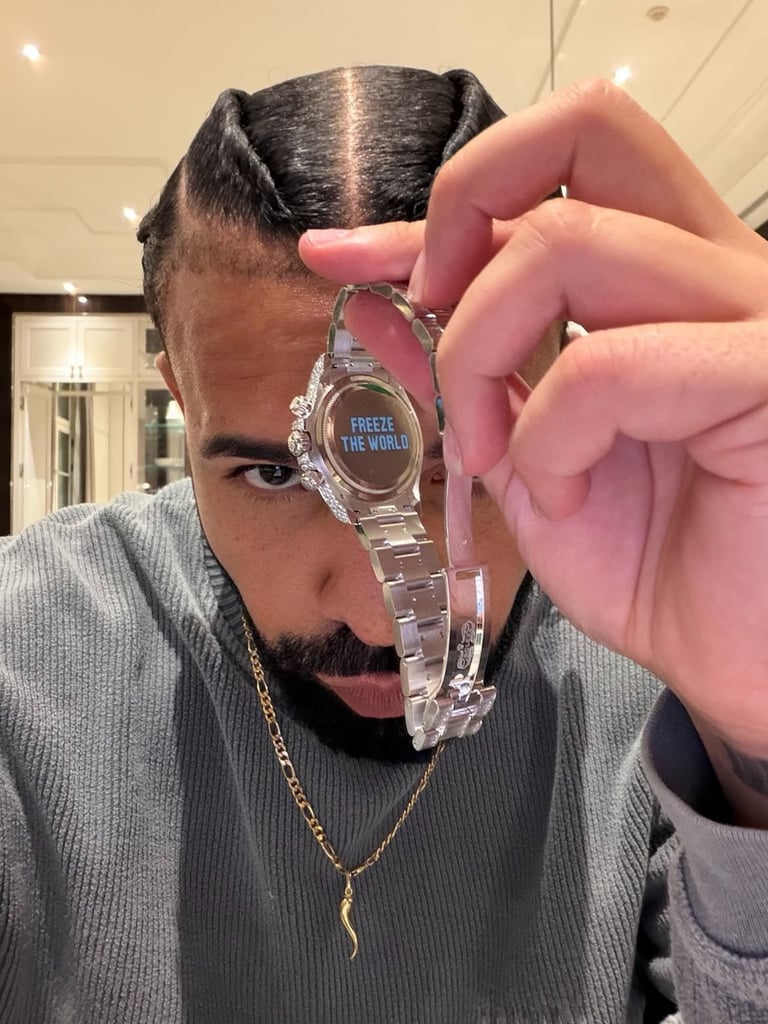 Person displaying a clear digital watch with text reading FREEZE THE WORLD, wearing gray ribbed shirt and gold chain necklace indoors.