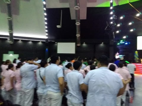 Multitud de personas con playeras blancas en evento con escenario