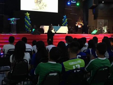 Audiencia en playeras verdes durante evento con escenario iluminado