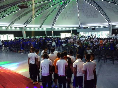 Gimnasio lleno de estudiantes con grupo de atletas jóvenes en tapete