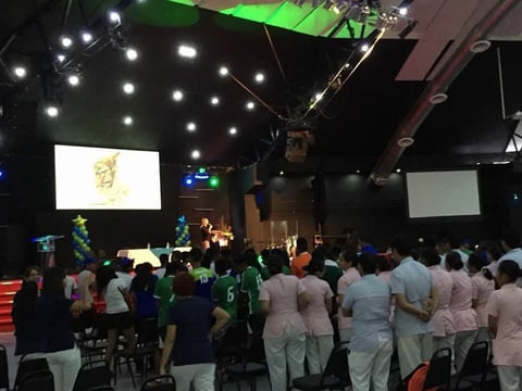 Audiencia grande con playeras blancas y verdes en evento con escenario iluminado