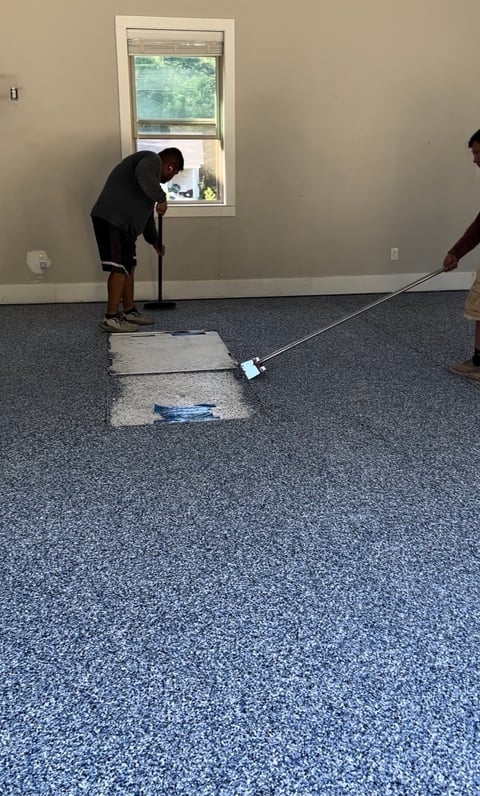 Person testing blue speckled flooring with tools in an empty room with beige walls and window