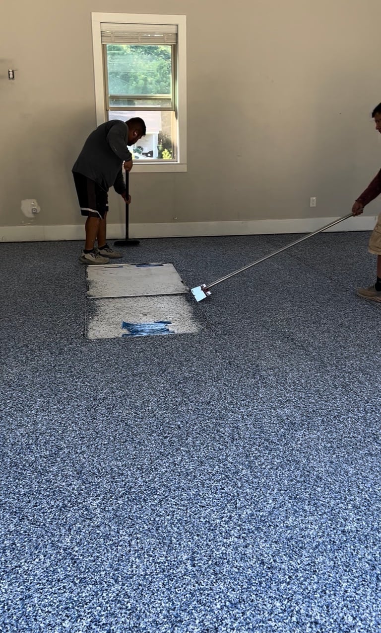 Person testing blue speckled flooring with tools in an empty room with beige walls and window