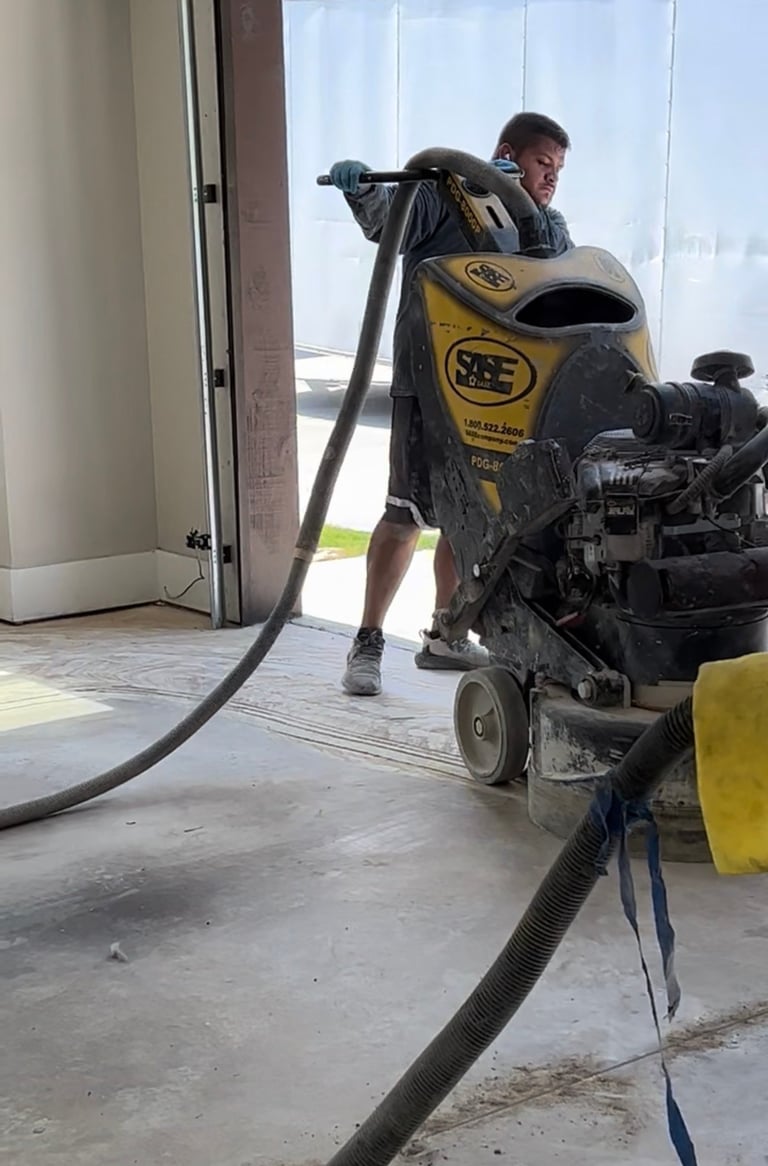 Worker operating yellow SAE concrete grinding machine on indoor floor with large hose