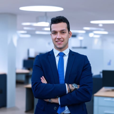 Professional man in navy blazer and blue tie standing with crossed arms in modern office environment