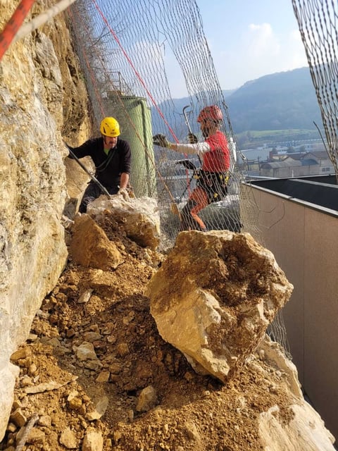 Rock climber in yellow helmet climbing artificial wall with safety net indoors, overlooking valley and mountains