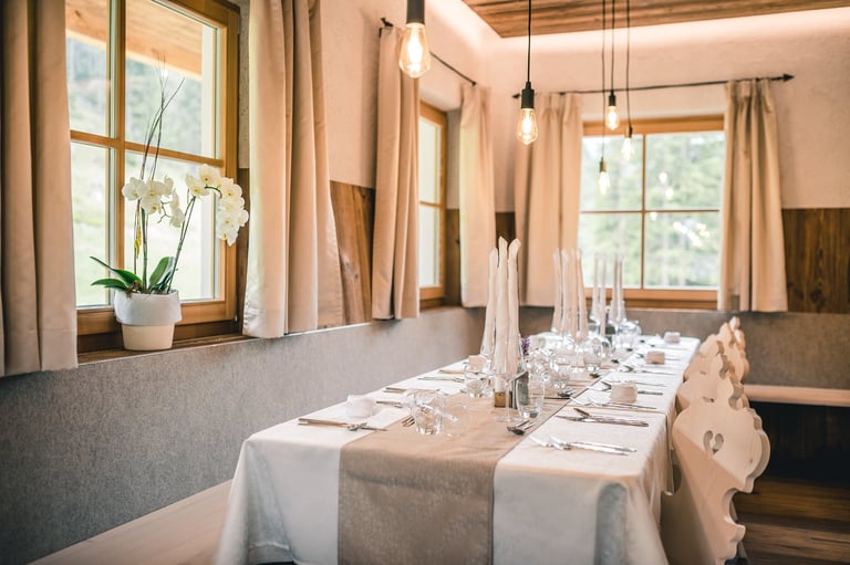 Elegant dining room with a long table set for a formal meal, featuring large windows, neutral tones, and hanging pendant lights.