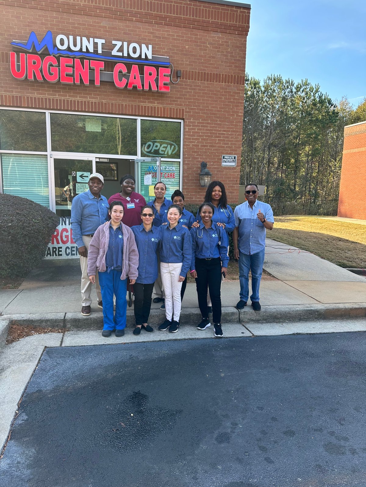 Wellspring Medical Center staff team posing outside the Mount Zion Urgent Care brick building with sign, wearing blue uniforms and casual clothing.