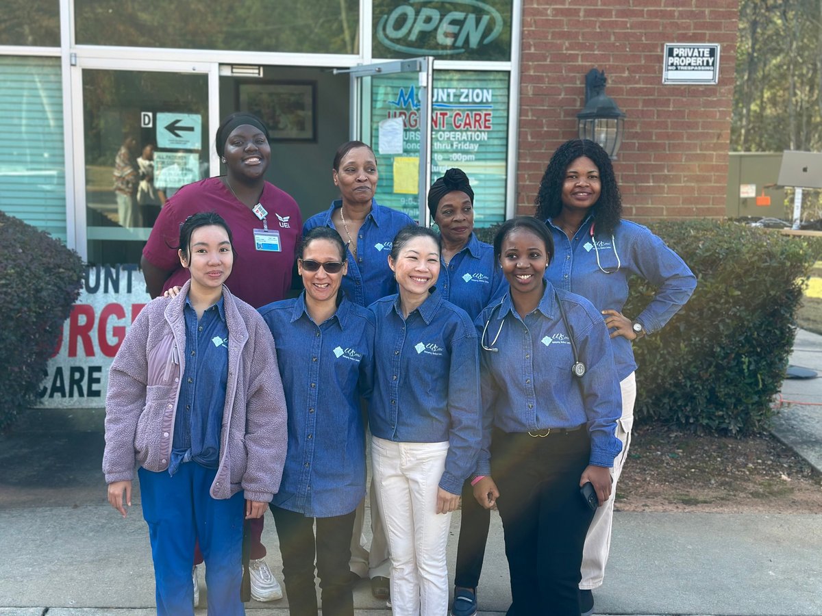 Group of healthcare workers in blue scrubs and white coats standing outside the Mount Zion Urgent Care medical clinic building in Jonesboro, GA.