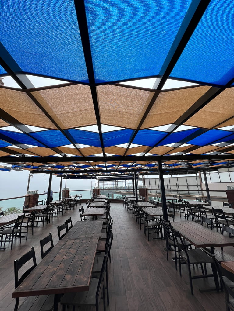 Pérgola metálica en Tijuana — Terraza en azotea con paneles de sombra retráctiles azules y beige sobre mesas de madera