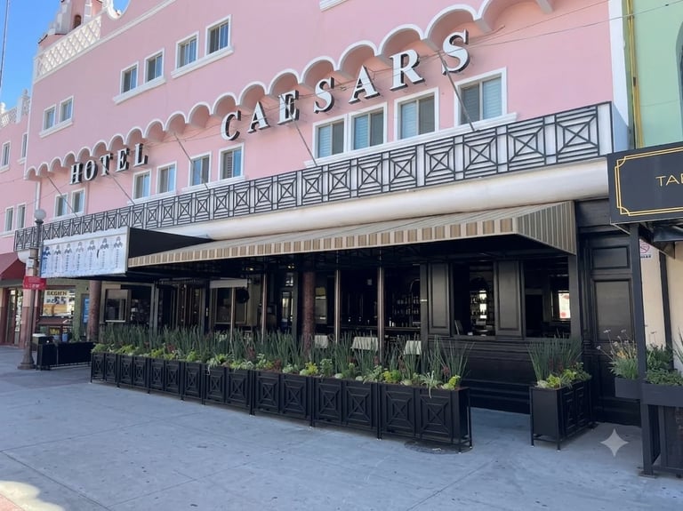 Edificio rosa del Hotel Caesars con toldo a rayas, fachada negra en planta baja, plantas y zona de estar al aire libre