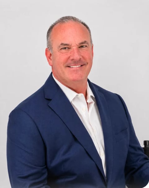 Professional headshot of a middle-aged man with gray hair wearing a dark blue blazer and white shirt against a gray background.