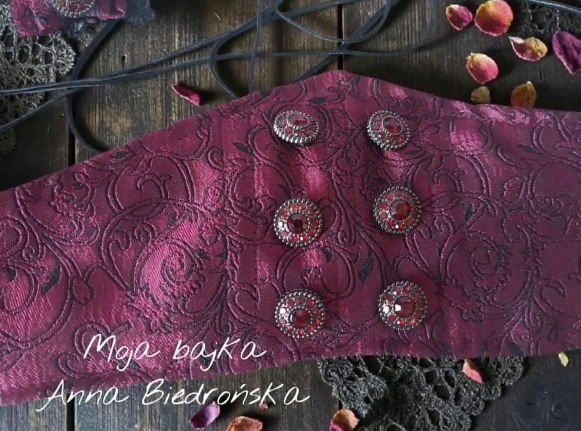 Purple ornate fabric with silver-studded embellishments and dried botanicals arranged on dark wooden surface with text overlay