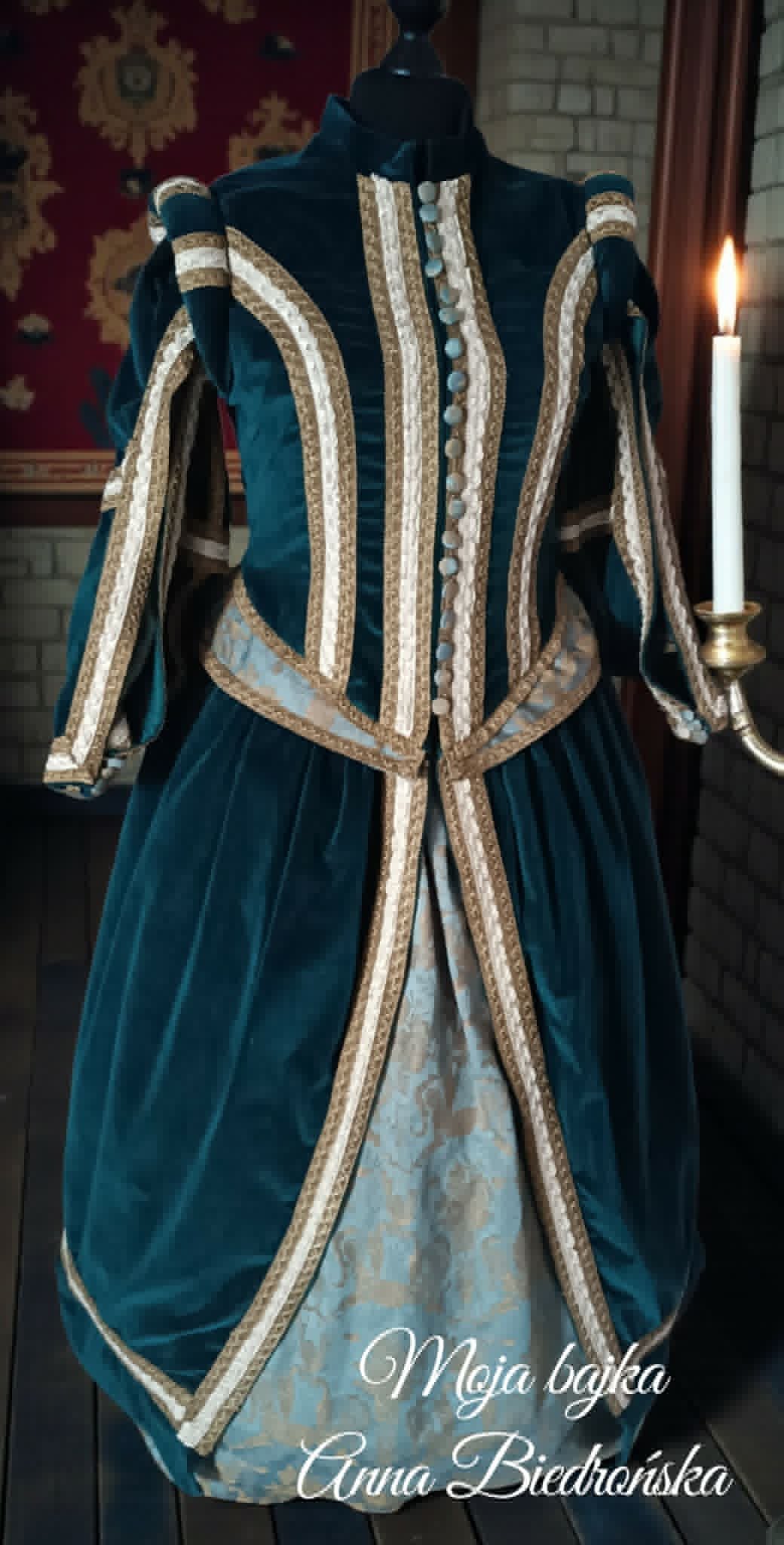 Medieval teal velvet gown with ornate gold and cream braided trim displayed on a dress form in period interior setting