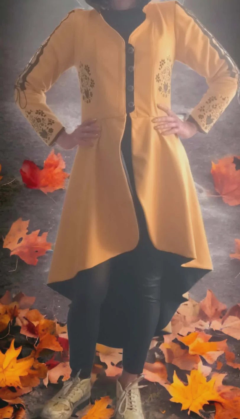 Person wearing a beige cardigan with decorative sleeves over dark pants, standing among autumn leaves