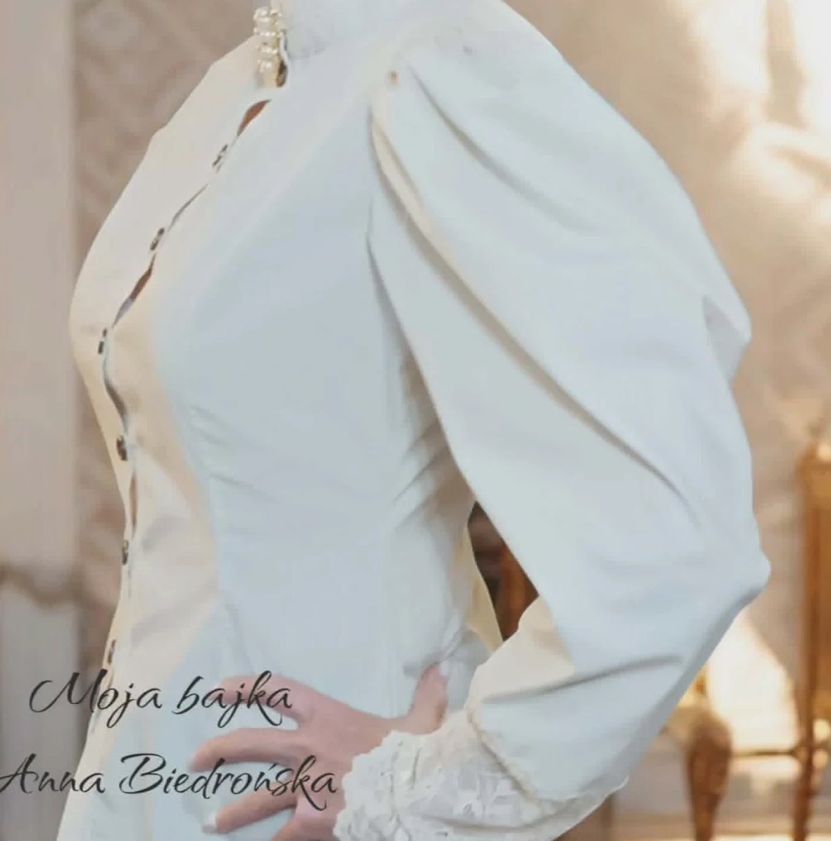 White hijab-style headwrap draping elegantly over shoulder with designer credit text overlay