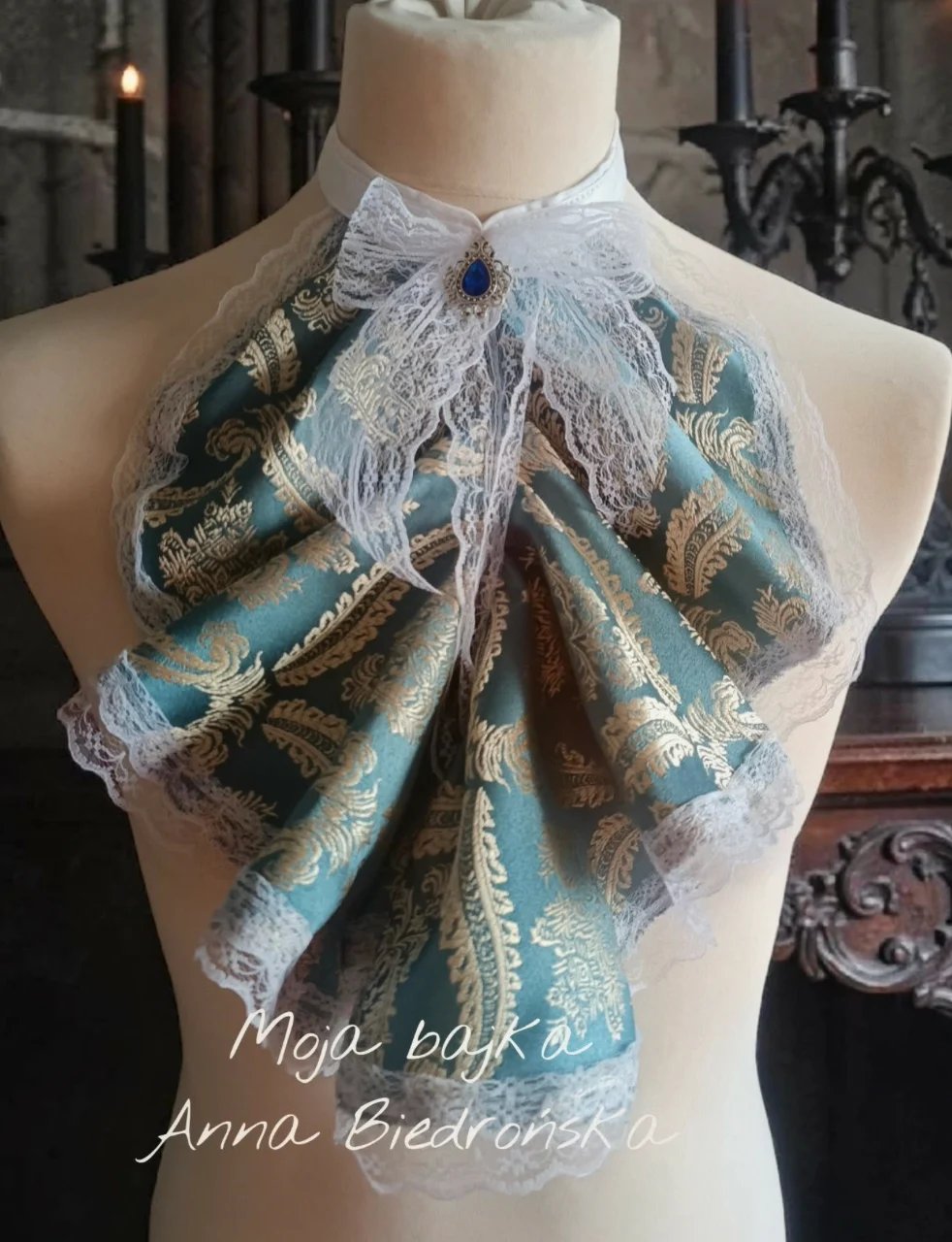 Mannequin wearing a teal and gold patterned fabric bow with white lace trim